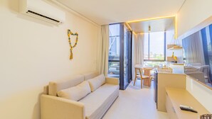 A modern living room with a sofa, a dining area with a table and chairs, and a kitchen counter with a sink and a window. - Cais Eco #310 - Ape com Piscina por Carpediem (Ipojuca)