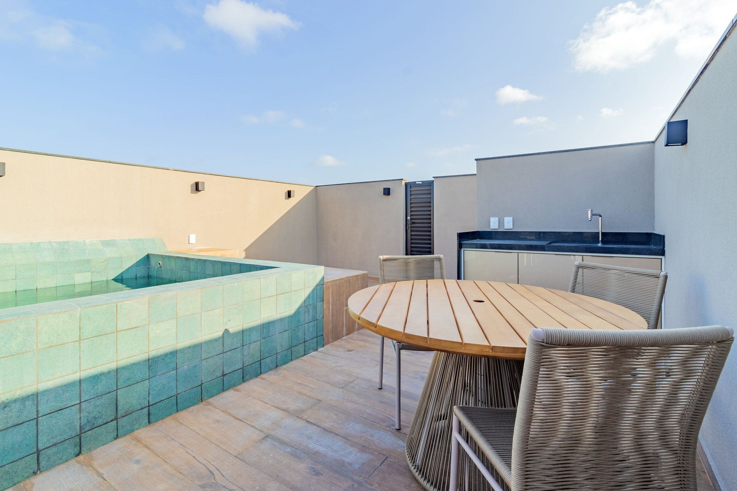 A rooftop terrace with a hot tub, a wooden table, and wicker chairs.