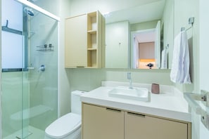 Ein modernes Badezimmer mit einer gläsernen Duschkabine, einem weißen Waschbecken und einem beigefarbenen Schrank.