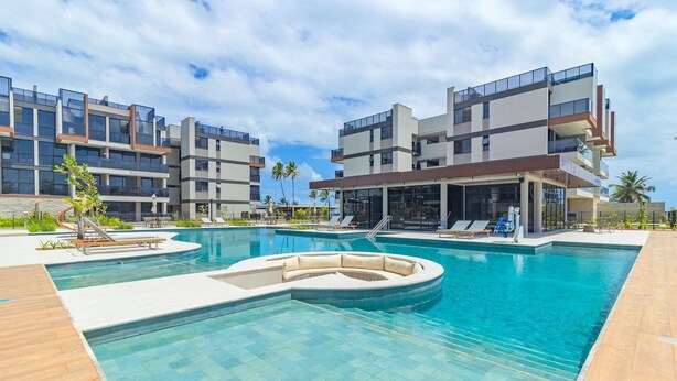 A modern hotel with a swimming pool, lounge chairs, and a covered area. - Cais Eco #310 - Ape com Piscina por Carpediem (Ipojuca)