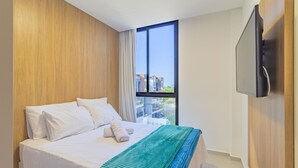 A hotel room with a large bed, a TV mounted on the wall, and a window with a city view. - Cais Eco #310 - Ape com Piscina por Carpediem (Ipojuca)