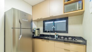 Eine kleine Küche mit einem Edelstahlkühlschrank, einer Mikrowelle, einem Gasherd und beigen Schränken.