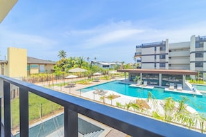A pool area with lounge chairs, a covered seating area, and a view of modern buildings. - Cais Eco #107 - Flatt With Balcony by Carpediem (Ipojuca)