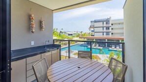 Ein Balkon mit Blick auf einen Pool, einem Tisch, Stühlen und einer hängenden Dekoration.