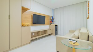 Ein modernes Wohnzimmer mit Flachbildfernseher, Glastisch, beiger Couch und eingebauten Holzregalen.