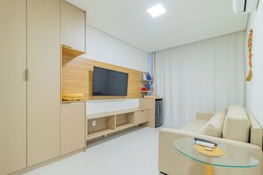 A modern living room with a flat-screen TV, a glass coffee table, a beige sofa, and built-in wooden shelving. - Cais Eco #107 - Flatt With Balcony by Carpediem (Ipojuca)