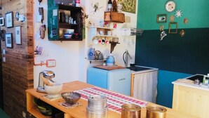 Cocina compacta con alacenas de madera, un refrigerador pequeño y diversos utensilios de cocina además de adornos en las paredes.