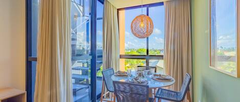 A dining area with a round table, chairs, and a view of greenery outside.