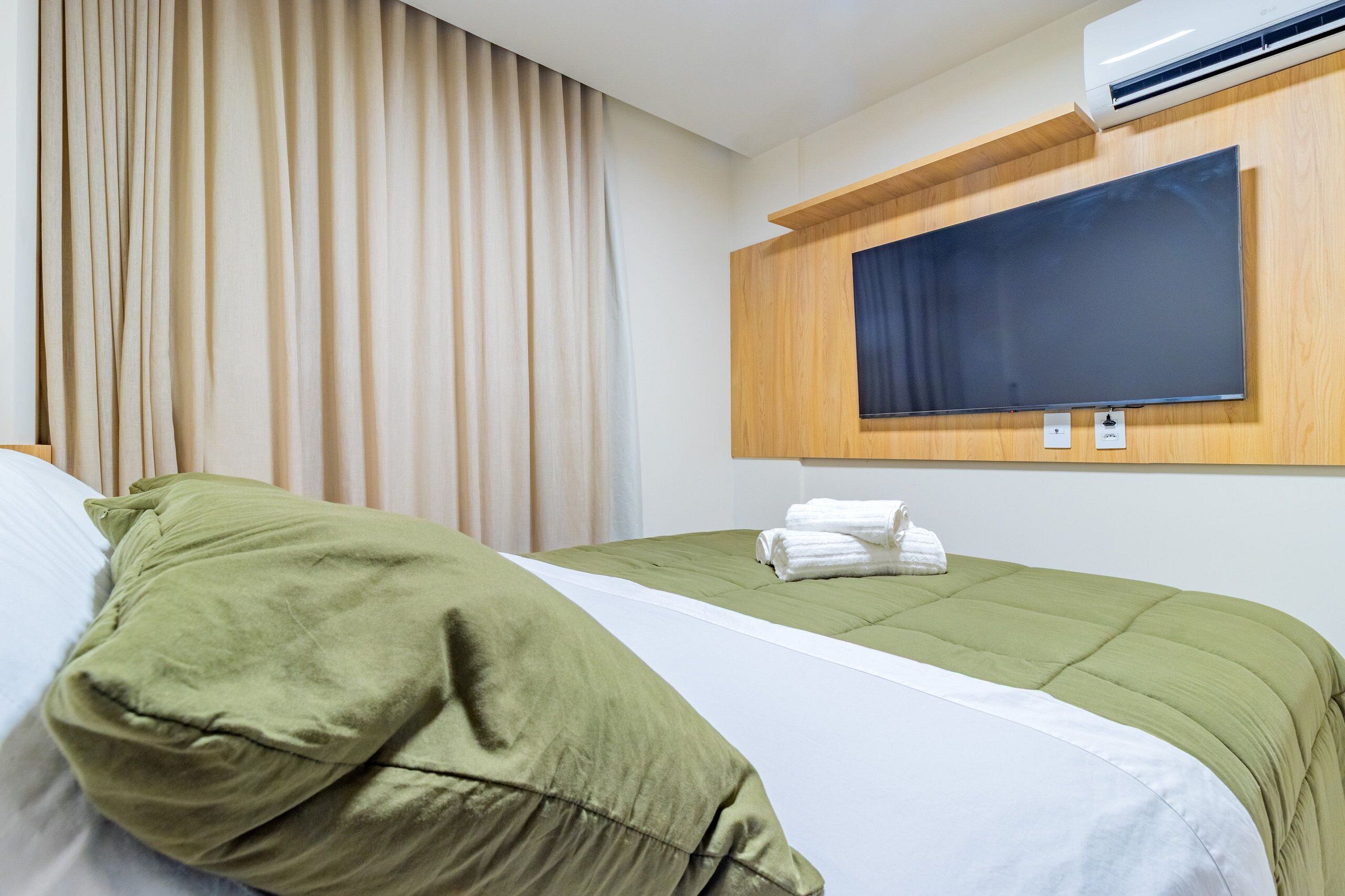 Hotellihuone, jossa on sänky, seinälle asennettu televisio ja ilmastointilaite.