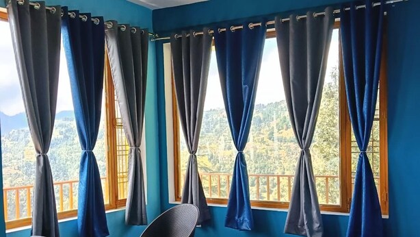 Ein Zimmer mit einem Bett, einem Tisch, zwei Stühlen und großen Fenstern mit Vorhängen.
