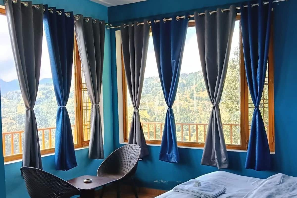A room with a bed, a table, two chairs, and large windows with curtains.