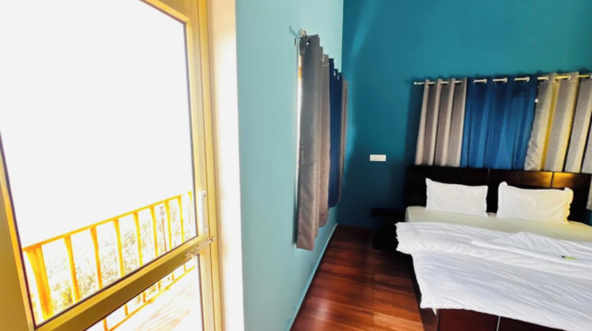 A room with a bed, a window with curtains, and a wooden floor.