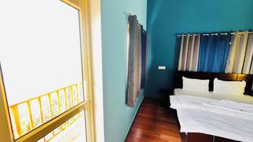 A room with a bed, a window with curtains, and a wooden floor.