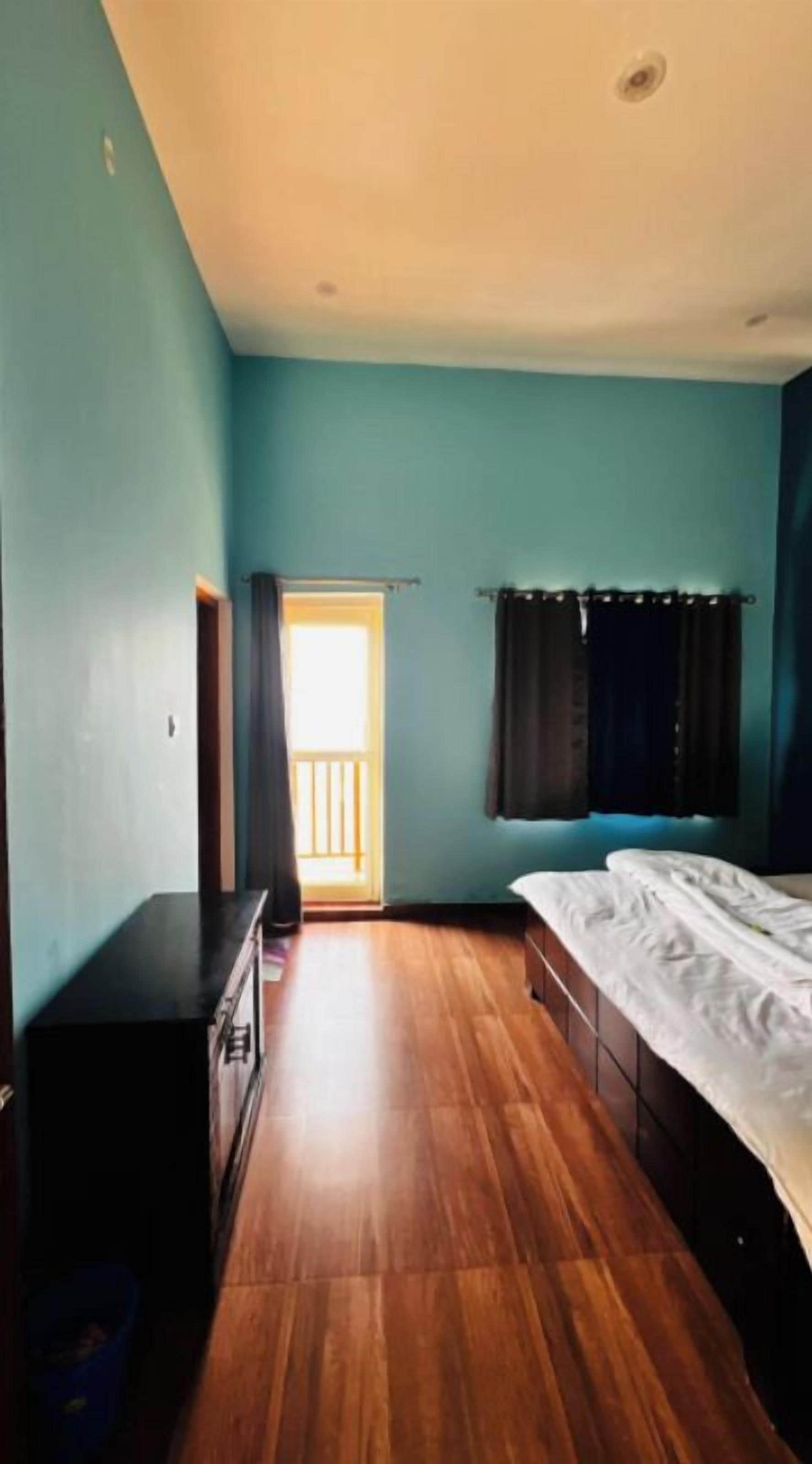 A bedroom with a wooden floor, a bed, a desk, and a window with curtains.