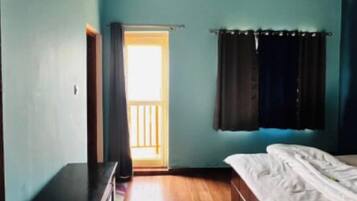 A bedroom with a wooden floor, a bed, a desk, and a window with curtains.