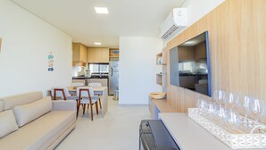 A modern, well-lit living area with a sofa, dining table, and chairs. A kitchen with cabinets and appliances is visible in the background. - Cais Eco #212 - Apartment on the Sand by Carpediem (Ipojuca)
