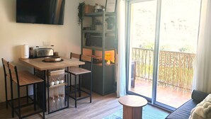 A modern kitchen with a flat-screen TV, wooden table, and chairs. There's a sliding glass door leading to a balcony with a view of a bamboo fence. - Ax-les-Thermes, cosy studio 4 pers and balcony : ski, hiking, thermal baths | All on foot (Savignac-les-Ormeaux)