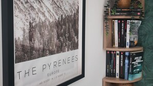 A framed picture of 'The Pyrenees' on a wall, a wooden bookshelf with books and a small plant, and a green textured wall. - Ax-les-Thermes, cosy studio 4 pers and balcony : ski, hiking, thermal baths | All on foot (Savignac-les-Ormeaux)