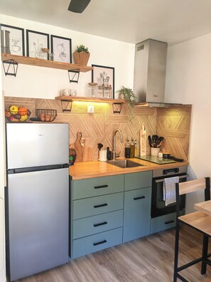 Eine moderne Küche mit Einbaukühlschrank, Spüle und Herd. Holzschränke, eine Arbeitsplatte und ein Deckenventilator sind vorhanden.