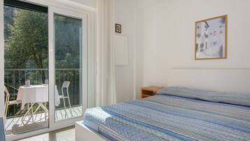 A bedroom with a bed, a window, a balcony with a table and chairs, and a framed picture on the wall.