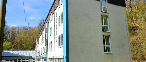 Un edificio de varios pisos con fachada azul y blanca, ventanas grandes y una bandera visible.