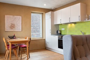 Cocina compacta con mesa, sillas, ventanal y salpicadero verde.