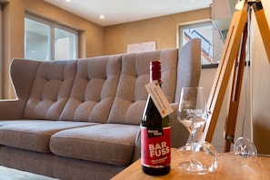 Una botella de vino, una copa y un caballete de madera en una habitación con sofá y ventana.