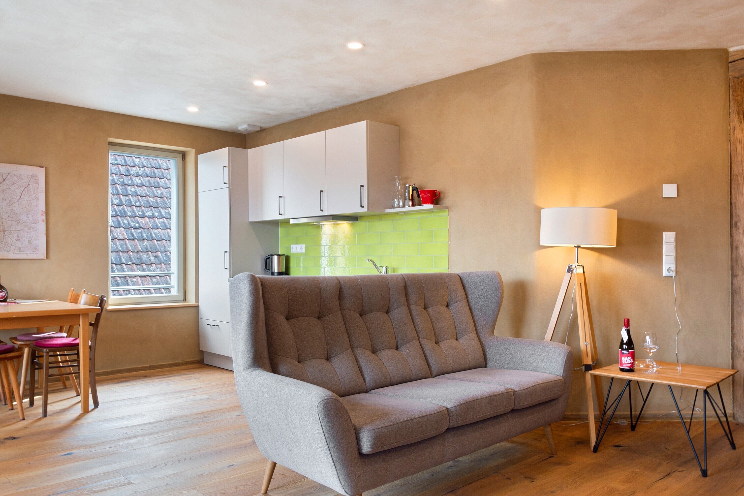 A living room with a sofa, a dining table with chairs, a kitchen area, and a lamp.
