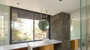 Une salle de bain moderne avec une grande fenêtre, un miroir rond, un lavabo blanc et un meuble en bois.