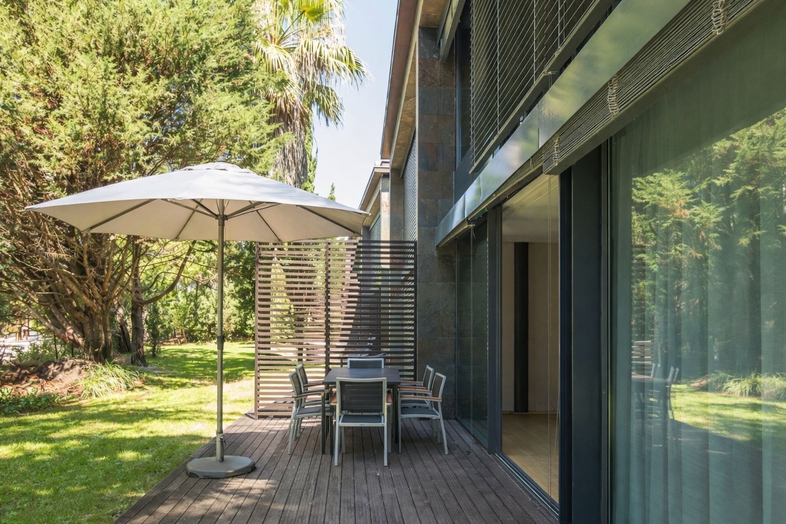 An outdoor patio with a table and chairs, a large umbrella, and a view of a forested area.