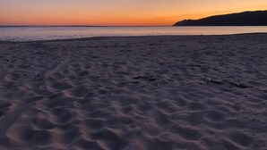 Une plage de sable avec de l’eau, une montagne lointaine et un coucher de soleil.