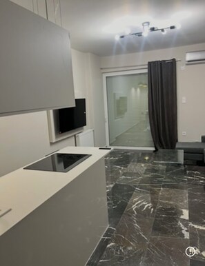 A modern living room with a flat-screen TV, a built-in kitchen counter, and a large window with curtains. - Spacious 2-bedroom Apartment in Paleo Faliro, Athens (Palaio Faliro)