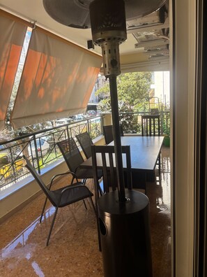 A covered outdoor seating area with a table and chairs, a metal pole, and a view of the street and greenery. - Spacious 2-bedroom Apartment in Paleo Faliro, Athens (Palaio Faliro)