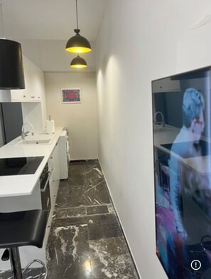 A narrow hallway with a white sink, a black pendant light, and a mirror reflecting a person. - Spacious 2-bedroom Apartment in Paleo Faliro, Athens (Palaio Faliro)
