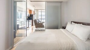 Et moderne hotelværelse med en stor seng, et siddeområde med en lænestol og udsigt over byen gennem store vinduer.