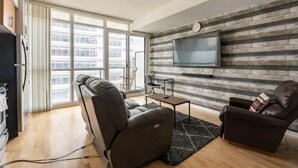 En moderne stue med sofa, lænestol og et fladskærms-tv monteret på en væg med stenvægsstruktur.