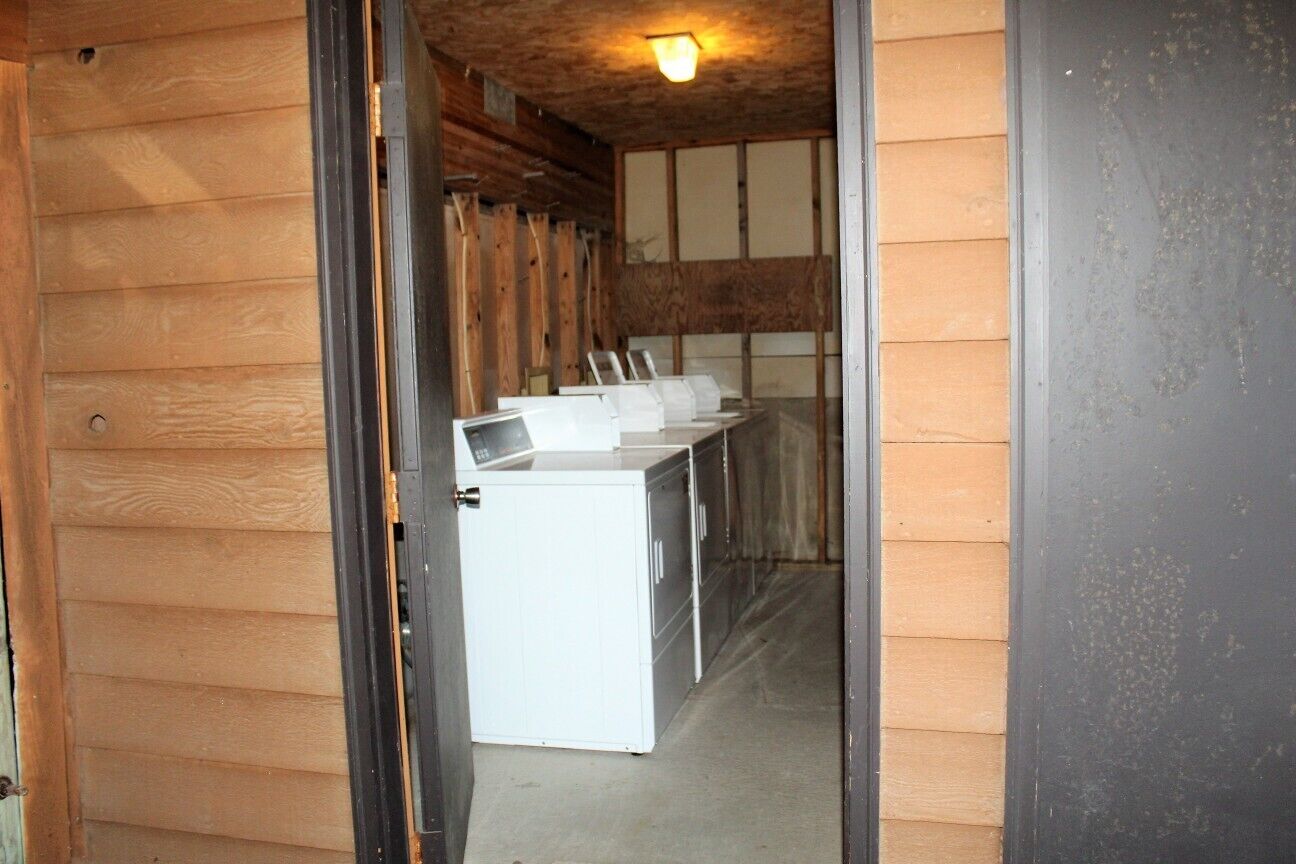 A laundry room with a washing machine and dryer, wooden walls, and a ceiling light.