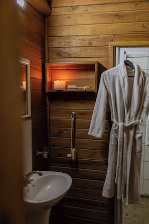 Ein Badezimmer mit Holzausstattung, das ein Waschbecken, einen Spiegel, einen Handtuchhalter und ein Regal mit einer Kerze zeigt.