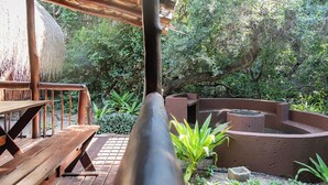 Una terraza de madera con bancos, rodeada de abundante vegetación y una estructura circular de piedra.