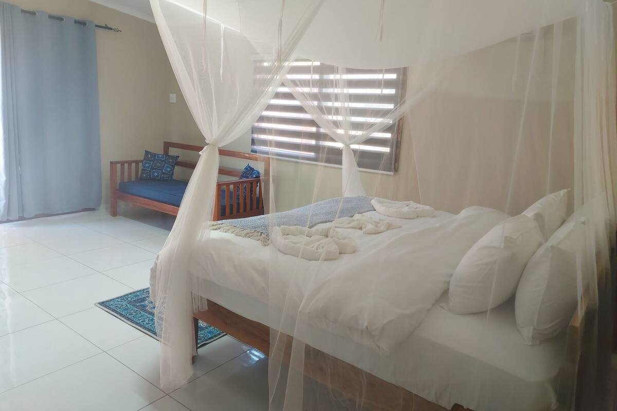 Une chambre à coucher avec un lit sous un dais, un banc en bois avec des coussins et une fenêtre avec des stores.