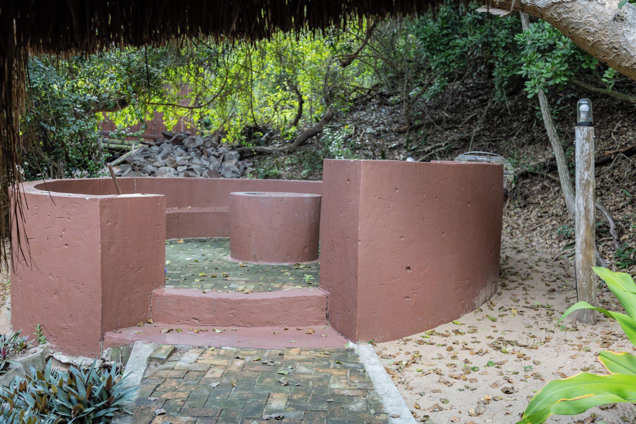 A concrete structure with steps leading up to a platform, surrounded by natural vegetation and a pile of rocks.