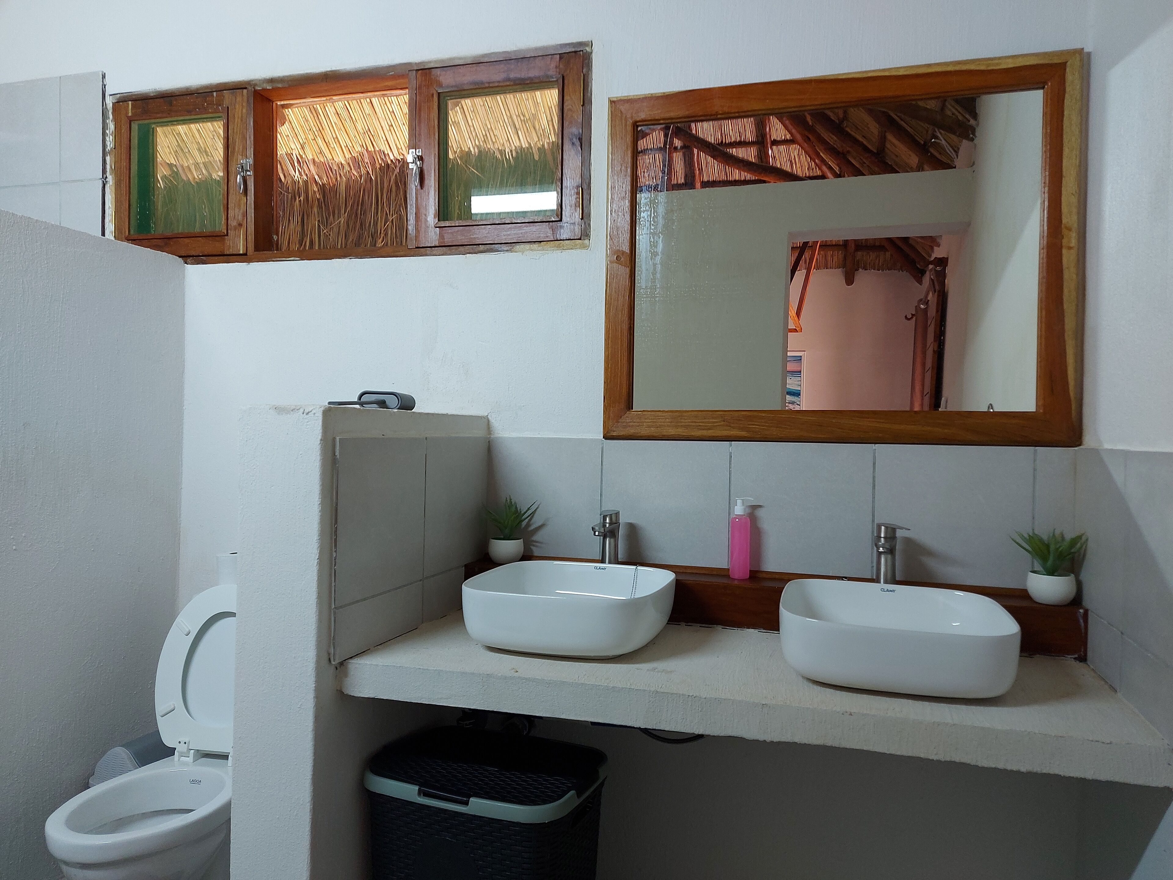 A bathroom with a toilet, two sinks, a mirror, and a window with a wooden frame.
