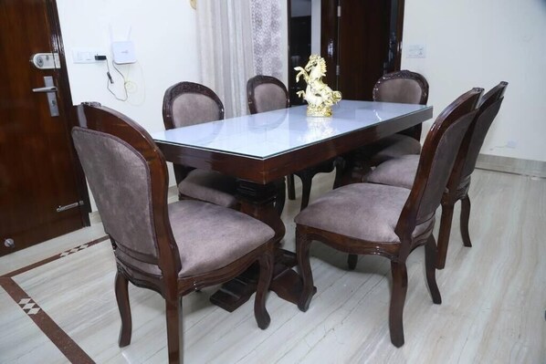 Un comedor con una mesa rectangular rodeada por seis sillas tapizadas, una estatua decorativa de un caballo dorado y un suelo de baldosas blancas.