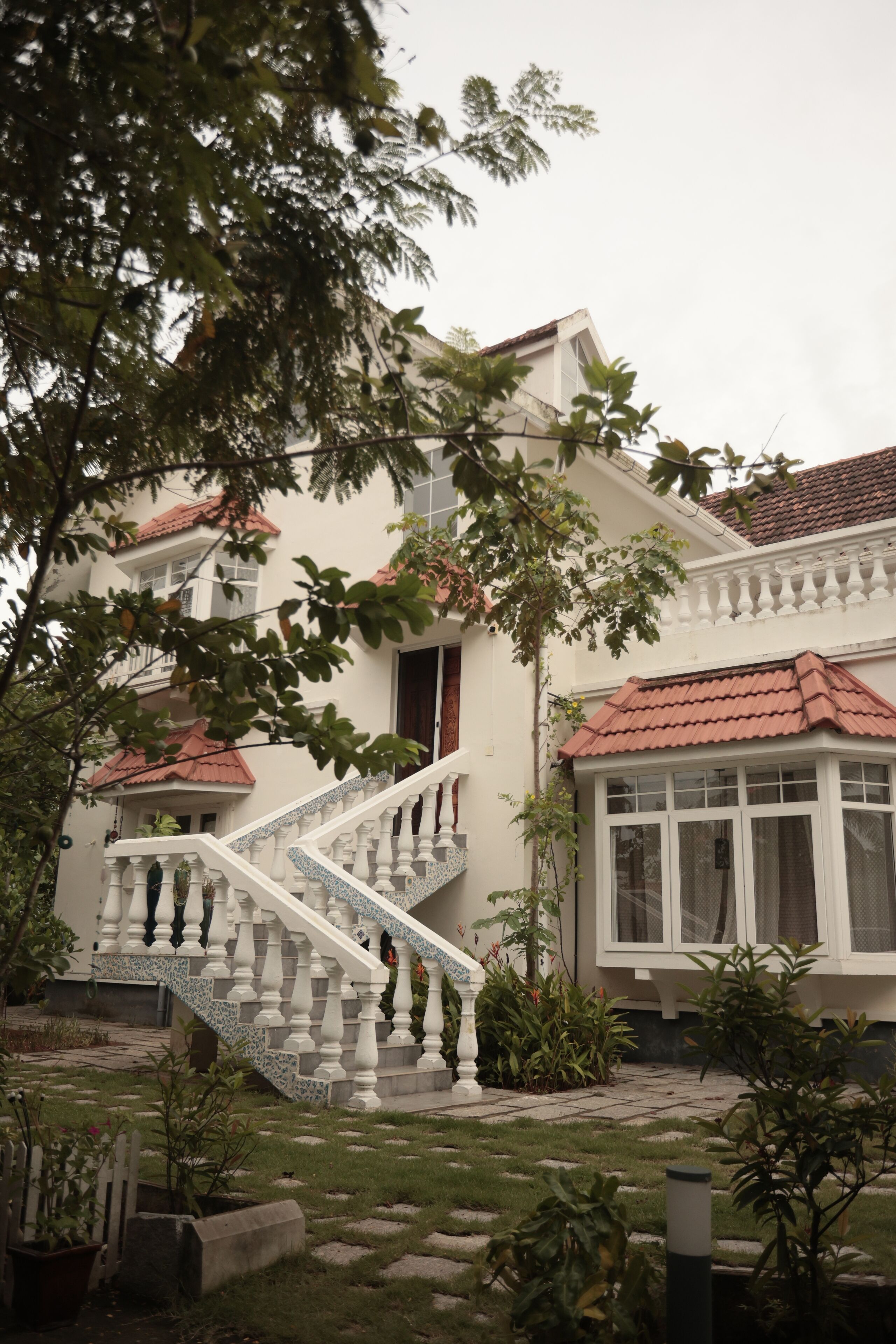 Uma casa com fachada branca, telhado de telhas vermelhas e uma escadaria branca que leva à entrada.