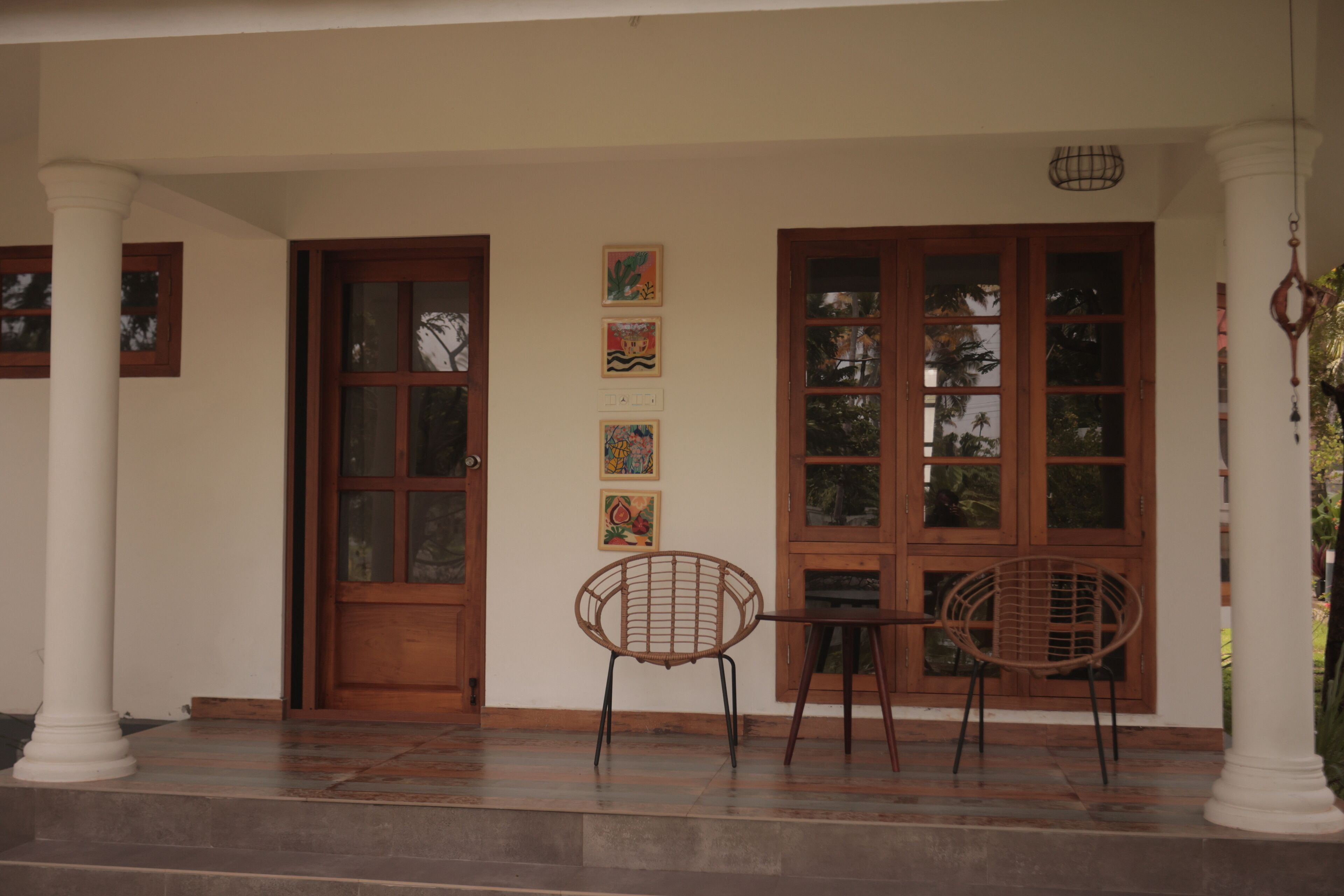 Un porche cubierto con puerta y ventanas de madera, una mesa con sillas y obras de arte en la pared.