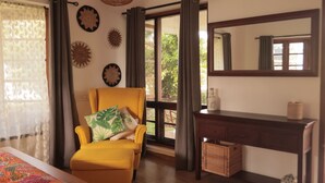 Una habitación con un sillón amarillo, un escritorio de madera, un espejo grande y decoración en la pared.
