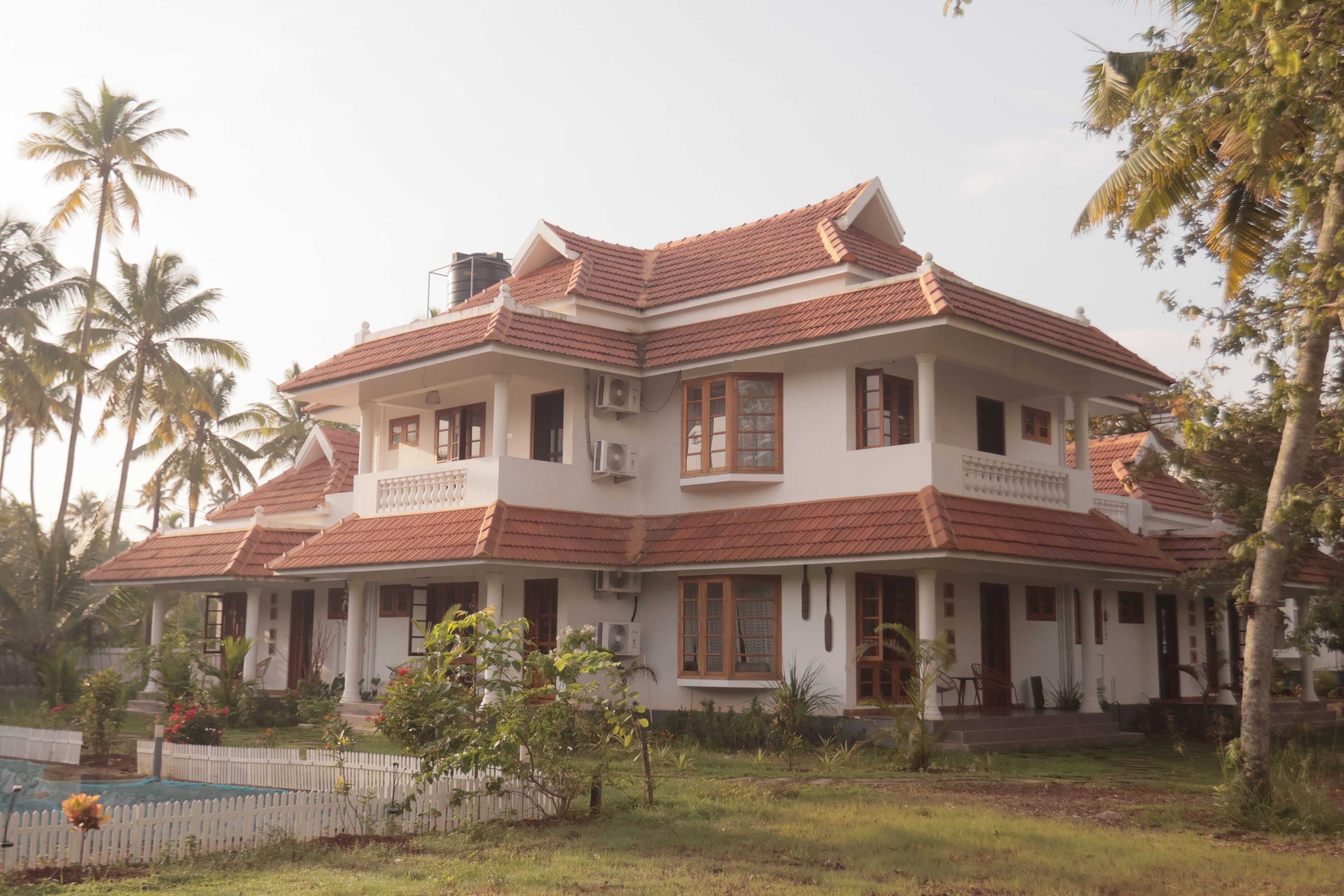 A two-story house with a red-tiled roof, white walls, and multiple windows.