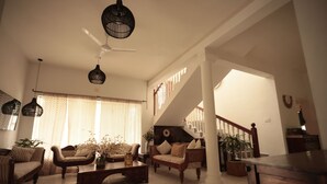Un salón espacioso con techo alto, una escalera y un amplio ventanal con cortinas.