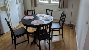 Een eetgedeelte met een ronde tafel, vier stoelen en een raam met gordijnen.