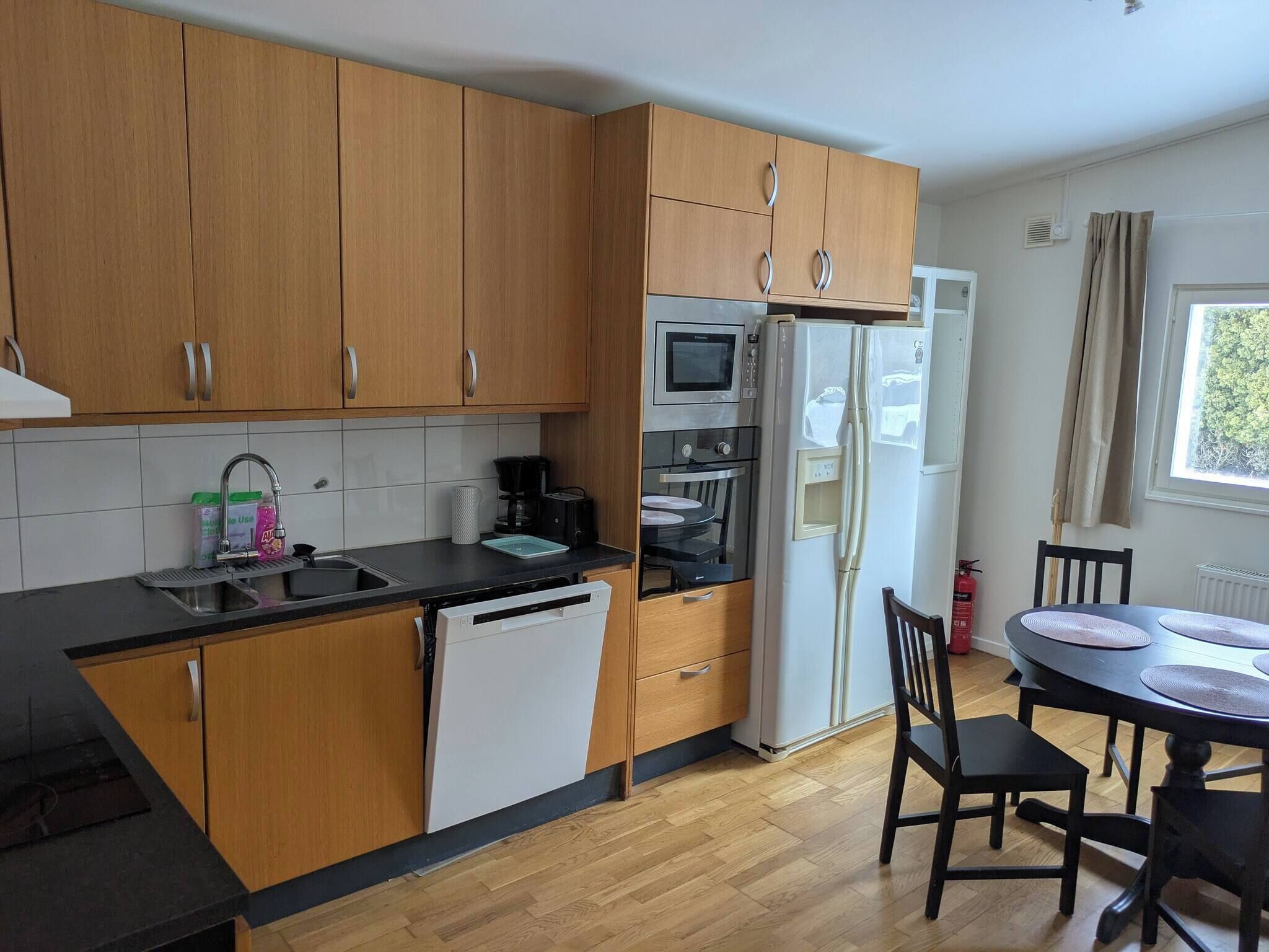 A modern kitchen with wooden cabinets, a built-in oven, a microwave, and a refrigerator.